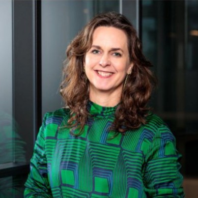 Portretfoto van een lachende vrouw met bruin krullend haar. Ze draagt een shirt met een groen-blauwe print.